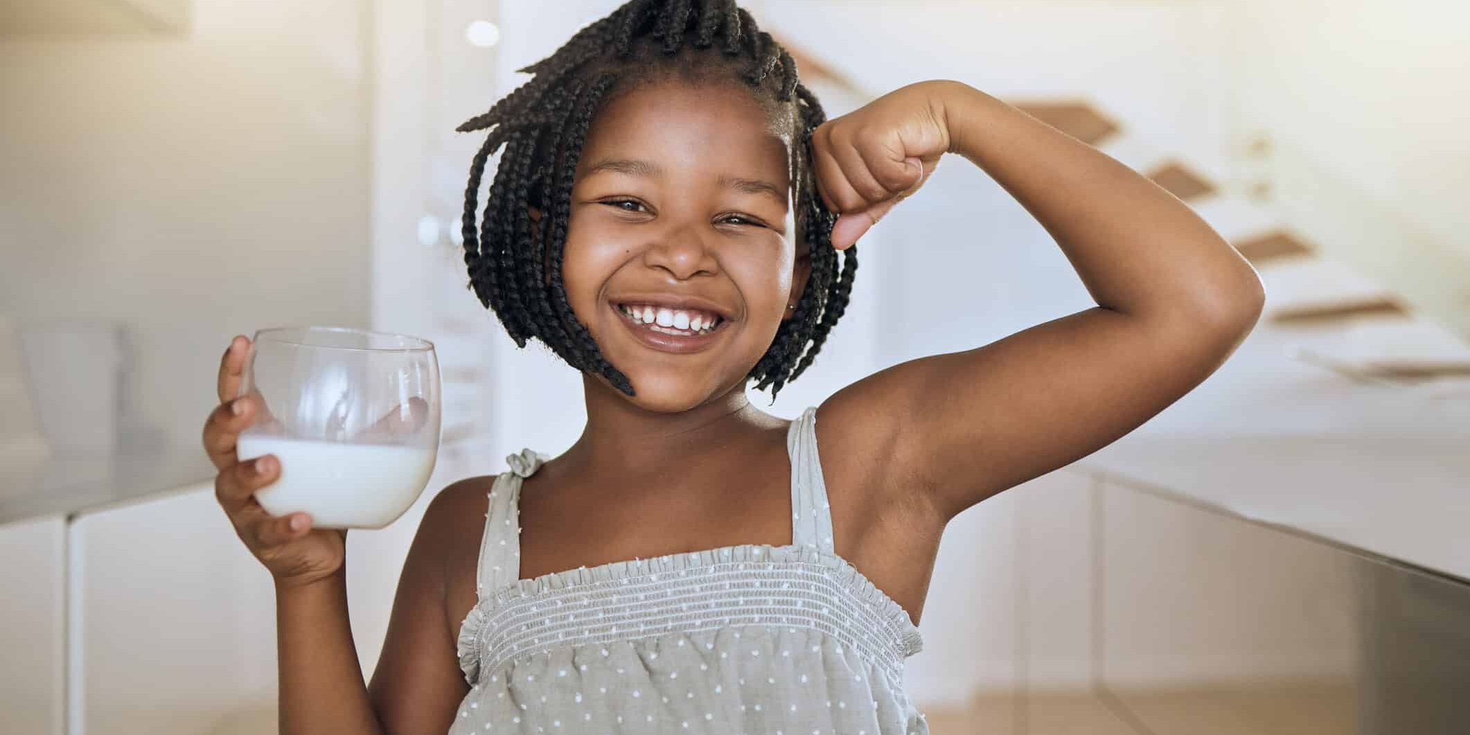 Milk, portrait and African girl with muscle from healthy drink for energy, growth and nutrition in the kitchen. Happy, smile and child flexing muscles from calcium in a glass and care for health healthy teeth